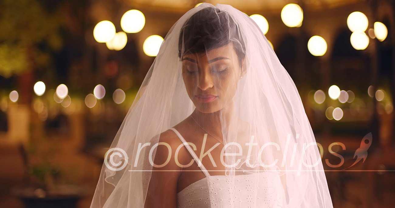Elegant bride posing outdoors in evening looking down veil covering face softly