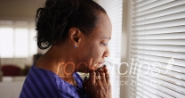An older black woman mournfully looks out her window