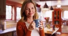 Woman drinking coffee or tea from mug inside contemporary kitchen