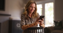 Caucasian woman messaging on smartphone seated in chair in living room