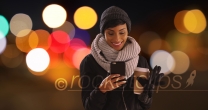 Cute black woman in her 20s texting on phone in urban setting with bokeh lights