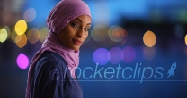 Black female in hijab texting on phone turning to smile at camera in evening