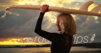 Mature white female surfer holding surfboard over head watching sunset at beach