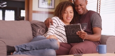 Millennial couple sitting on couch watching movie on their tablet computer