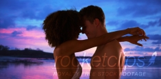 African woman with arms around boyfriend under pink and blue sky.