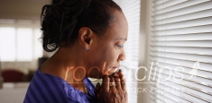 An older black woman mournfully looks out her window