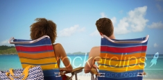 Close-up of couple sitting on beach chairs looking at water horizon.