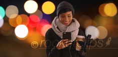 Cute black woman in her 20s texting on phone in urban setting with bokeh lights