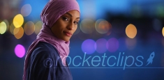 Black female in hijab texting on phone turning to smile at camera in evening