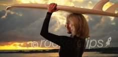 Mature white female surfer holding surfboard over head watching sunset at beach