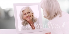 Lovely Caucasian senior lady looking at herself in mirror in clean white setting